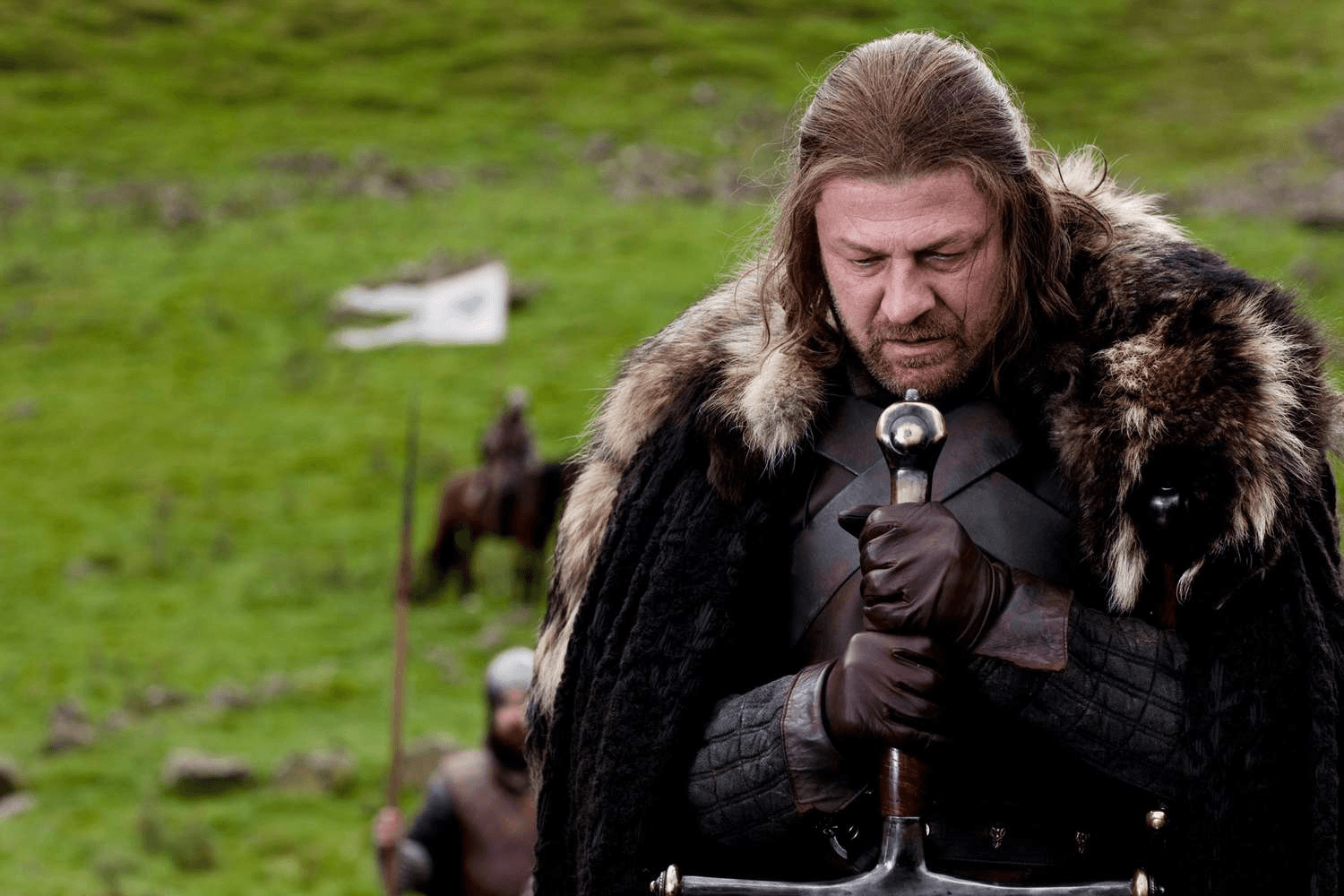 Ned Stark holding a big sword and looking down.